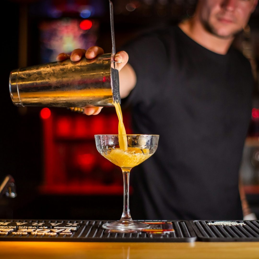 Un barman en train de verser un cocktail dans un verre à pied, en contexte professionnel de bar