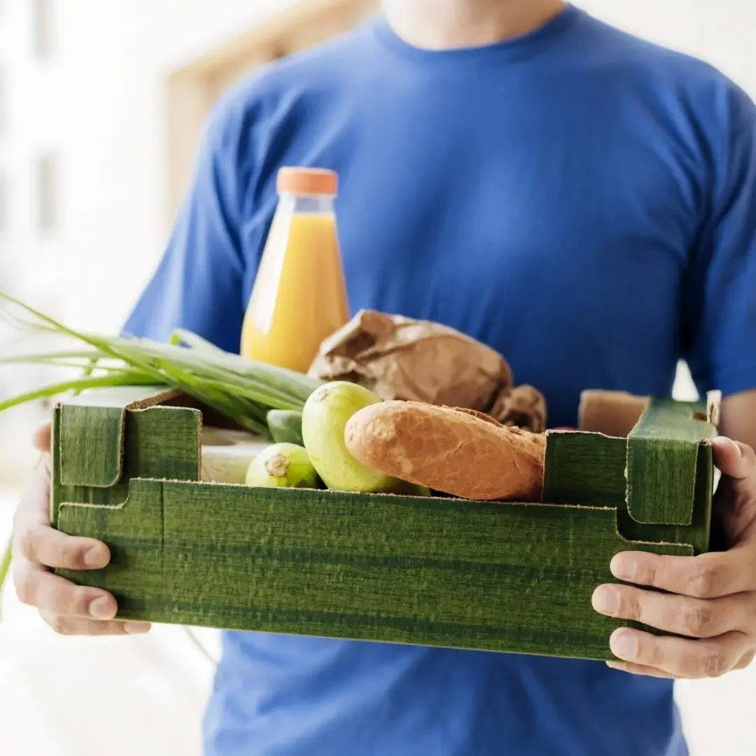 Personne livrant un panier de courses contenant pain, légumes et jus de fruits